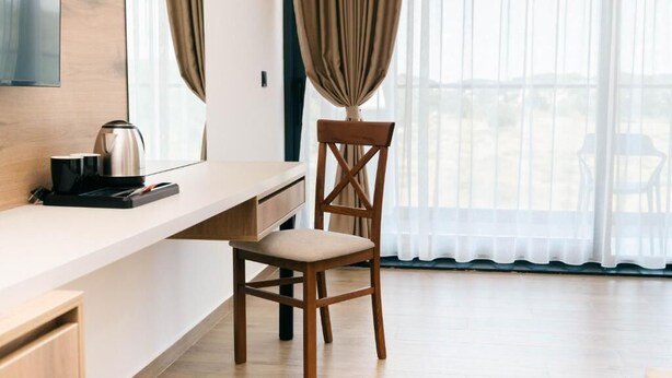 Una habitación moderna con un escritorio de madera, una silla, un hervidor de agua y un ventanal con cortinas.