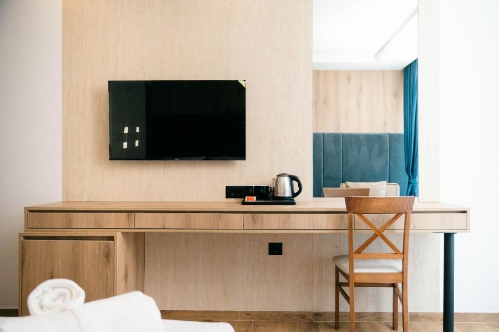 Una habitación de hotel moderna con un escritorio de madera, un televisor montado en la pared, una silla y una cama con una toalla enrollada.