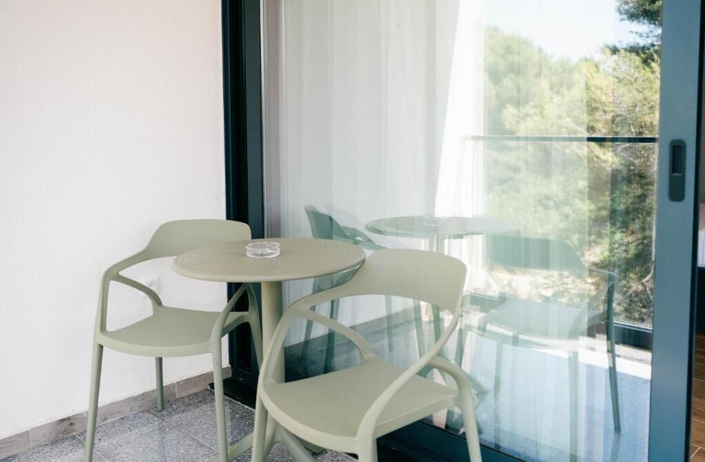 A balcony with two chairs and a small table, a glass door, and a view of greenery.