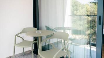A balcony with two chairs and a small table, a glass door, and a view of greenery.