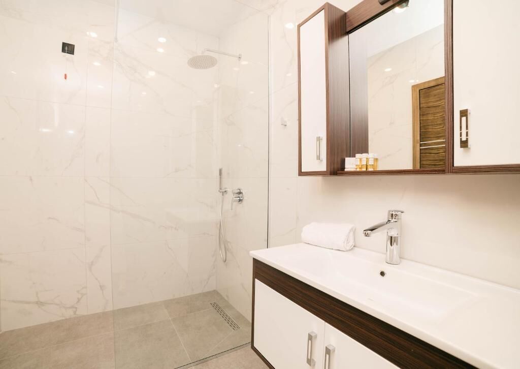 A modern bathroom with a glass-enclosed shower, a white vanity with a mirror, and a wooden cabinet.