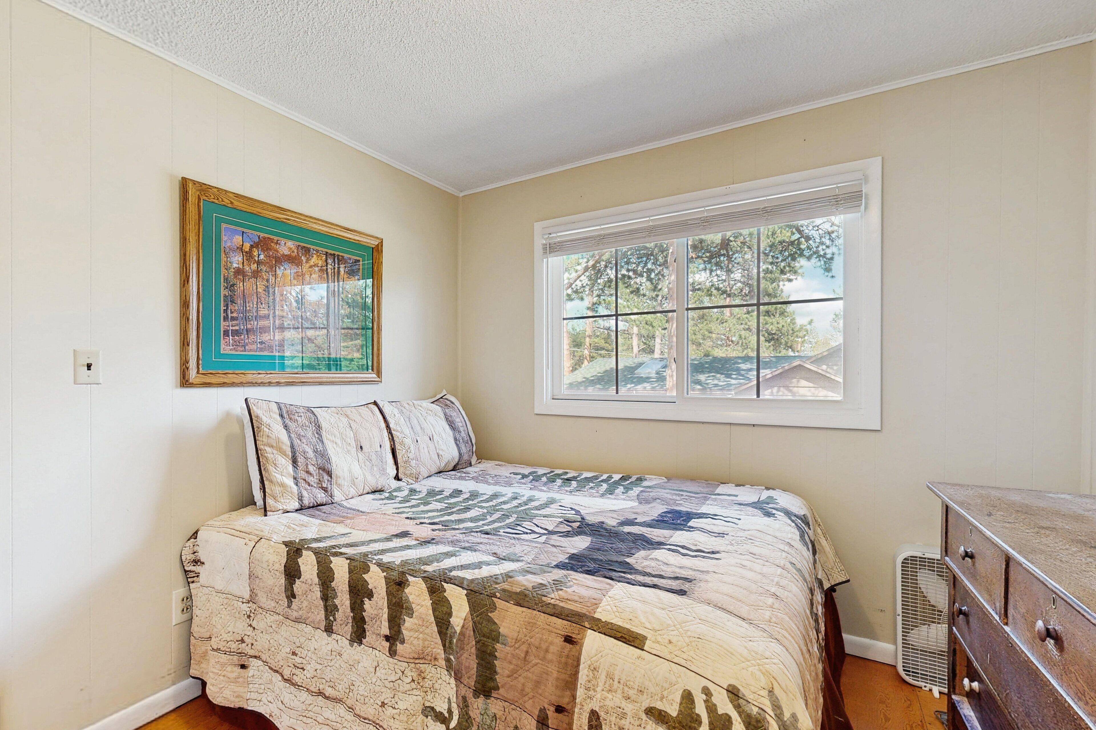 A bedroom with a bed, a window, a dresser, and a framed picture on the wall.
