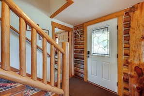 Una escalera de madera conduce a una habitación con pared de troncos y una puerta con vidriera.