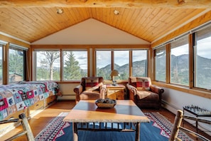 Ein Zimmer mit Holzbalkendecke, großen Fenstern, einem Bett, zwei Sesseln, einem Tisch mit Schüssel und einem Schachbrett.
