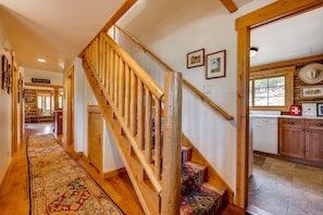 Una escalera de madera con un tapete estampado que conduce a una zona de cocina con armarios de madera y un ventanal.
