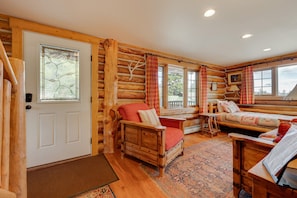 Ein Holzblockhaus-Interieur mit einer Holztür, einem rot gepolsterten Sessel, einer Holzbank und einem gemusterten Teppich.