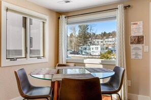 A room with a round glass table, two leather chairs, a window with curtains, and a view of a residential area. - Remodeled, Dog-friendly Cabin in Heart of Downtown With Patio (Estes Park)