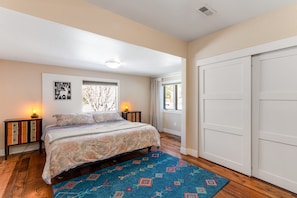 A bedroom with a bed, a window, a door, and a nightstand with a lamp. - Remodeled, Dog-friendly Cabin in Heart of Downtown With Patio (Estes Park)