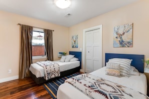 Une chambre avec deux lits, une fenêtre avec des rideaux, une porte et deux tableaux accrochés au mur.