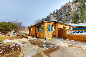 A log cabin with a stone pathway leading to the entrance, a wooden fence, and a mountain backdrop. - Remodeled, Dog-friendly Cabin in Heart of Downtown With Patio (Estes Park)