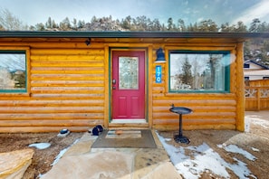 Une cabane en rondins avec une porte rouge, un paillasson et une plaque indiquant le numéro de la maison.