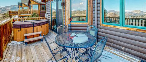 A wooden cabin with a deck, a hot tub, and a table with chairs.