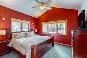 A bedroom with a bed, nightstands, a dresser, a ceiling fan, and windows with a view of trees. - Two BR Condo w/ Brand NEW HOT TUB and Great Views! (Estes Park)
