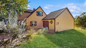A two-story wooden house with a front door, windows, and a small porch. - Spacious Cabin With Stunning Views, Wifi, Fully Stocked Kitchen & W/D (Drake)