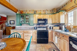 A kitchen with wooden cabinets, a black microwave, a stove, and a sink.