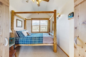A wooden four-poster bed with a view of the desert through a large window.