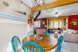 A dining area with a wooden table and turquoise chairs, a ceiling fan, and a red wall with a framed picture.