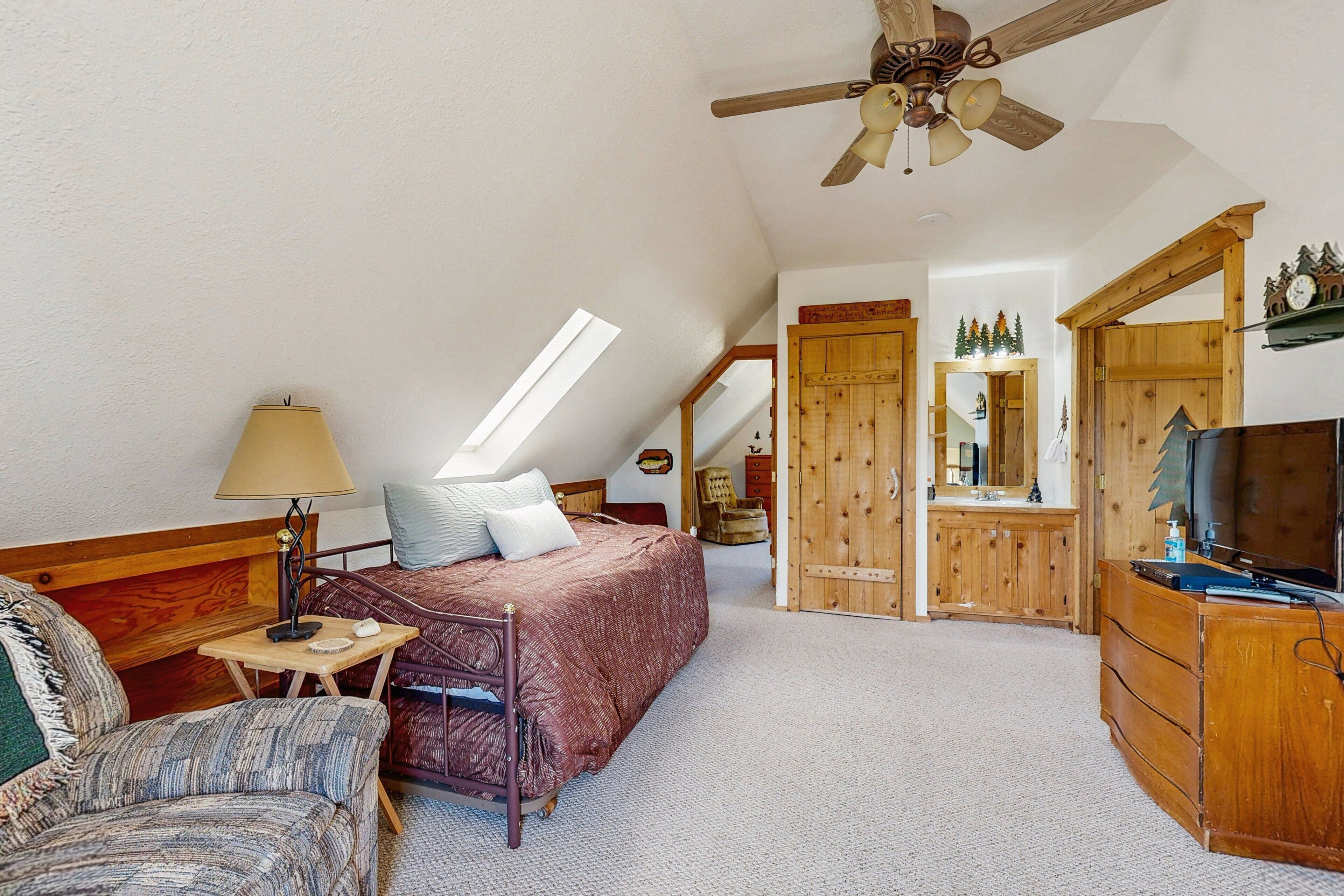 Une chambre à coucher comprenant un lit, un bureau, une chaise, une commode, un miroir et un ventilateur de plafond.
