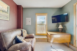 A living room with a leather couch, a wooden desk, a television, and a window with a view. - Spacious Cabin With Stunning Views, Wifi, Fully Stocked Kitchen & W/D (Drake)