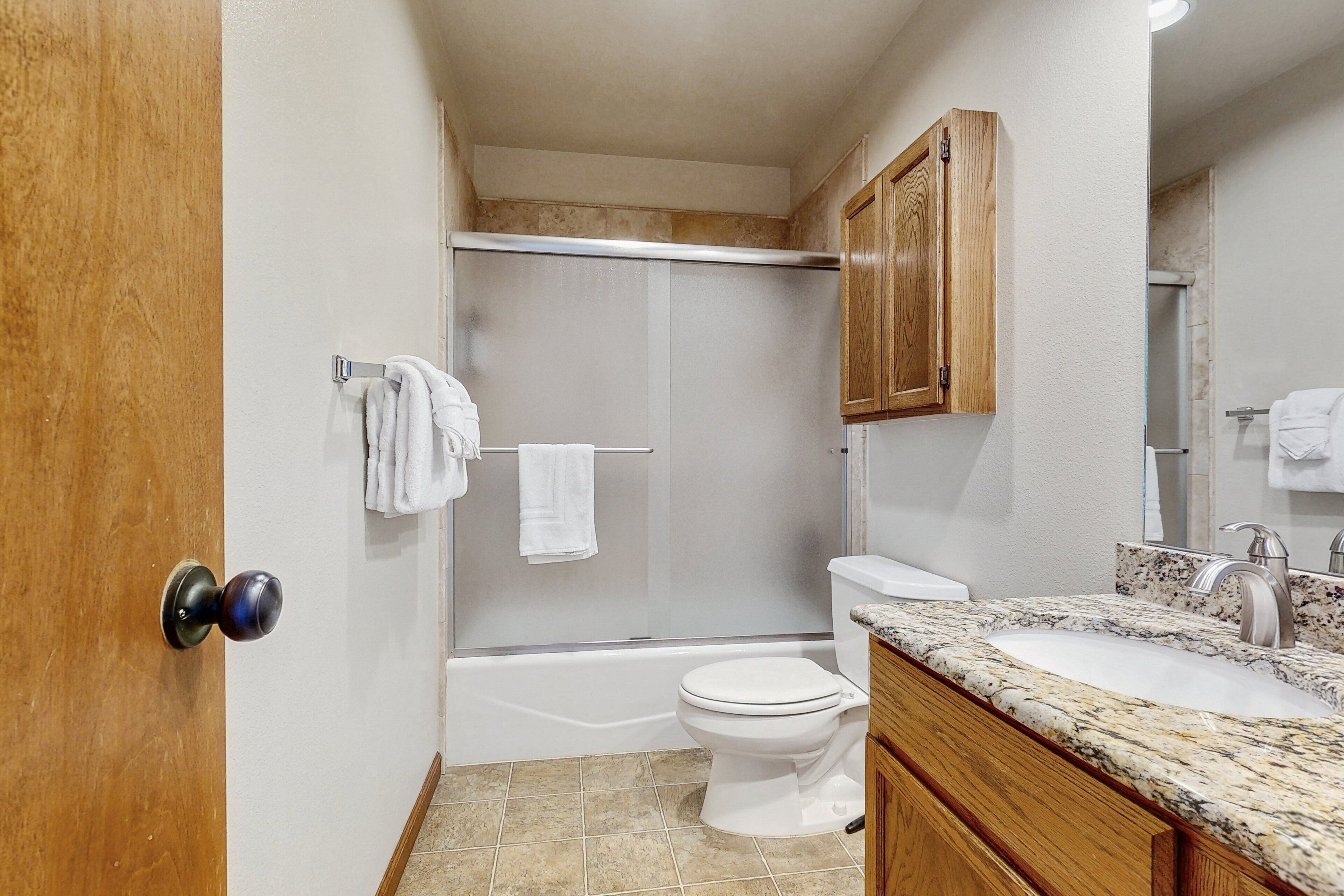 A bathroom with a shower, toilet, sink, and wooden cabinets.