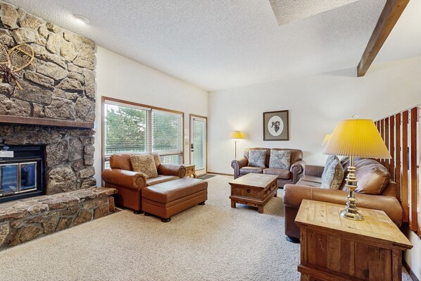 A living room with a stone fireplace, leather sofas, a wooden coffee table, and a lamp on a wooden side table. - Comfortable Home With Breathtaking Mountain Views and High-speed Wifi (Estes Park)