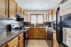 A kitchen with wooden cabinets, a stove, a refrigerator, and a window with blinds. - Comfortable Home With Breathtaking Mountain Views and High-speed Wifi (Estes Park)