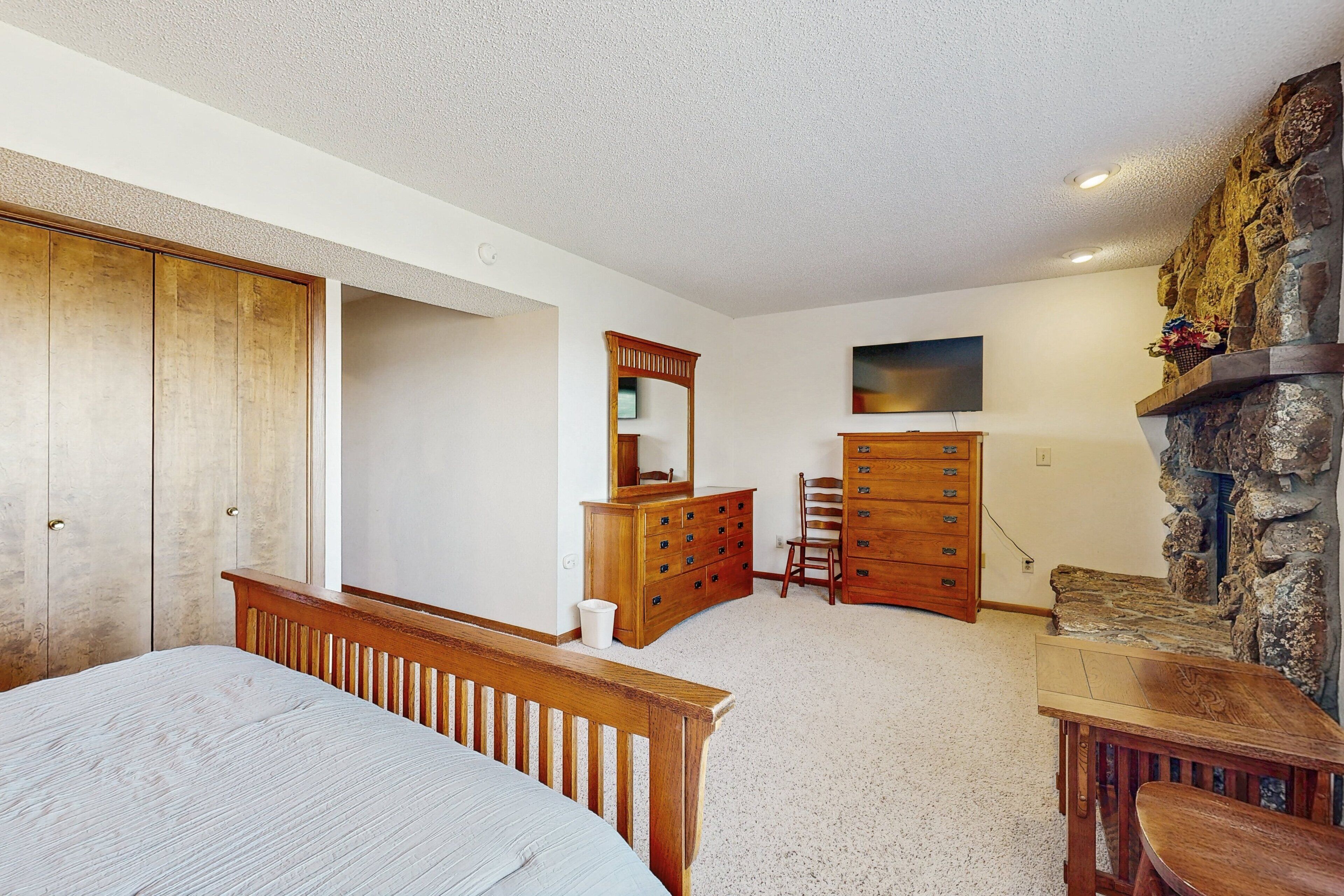 A bedroom with a bed, dresser, chair, and a stone wall.
