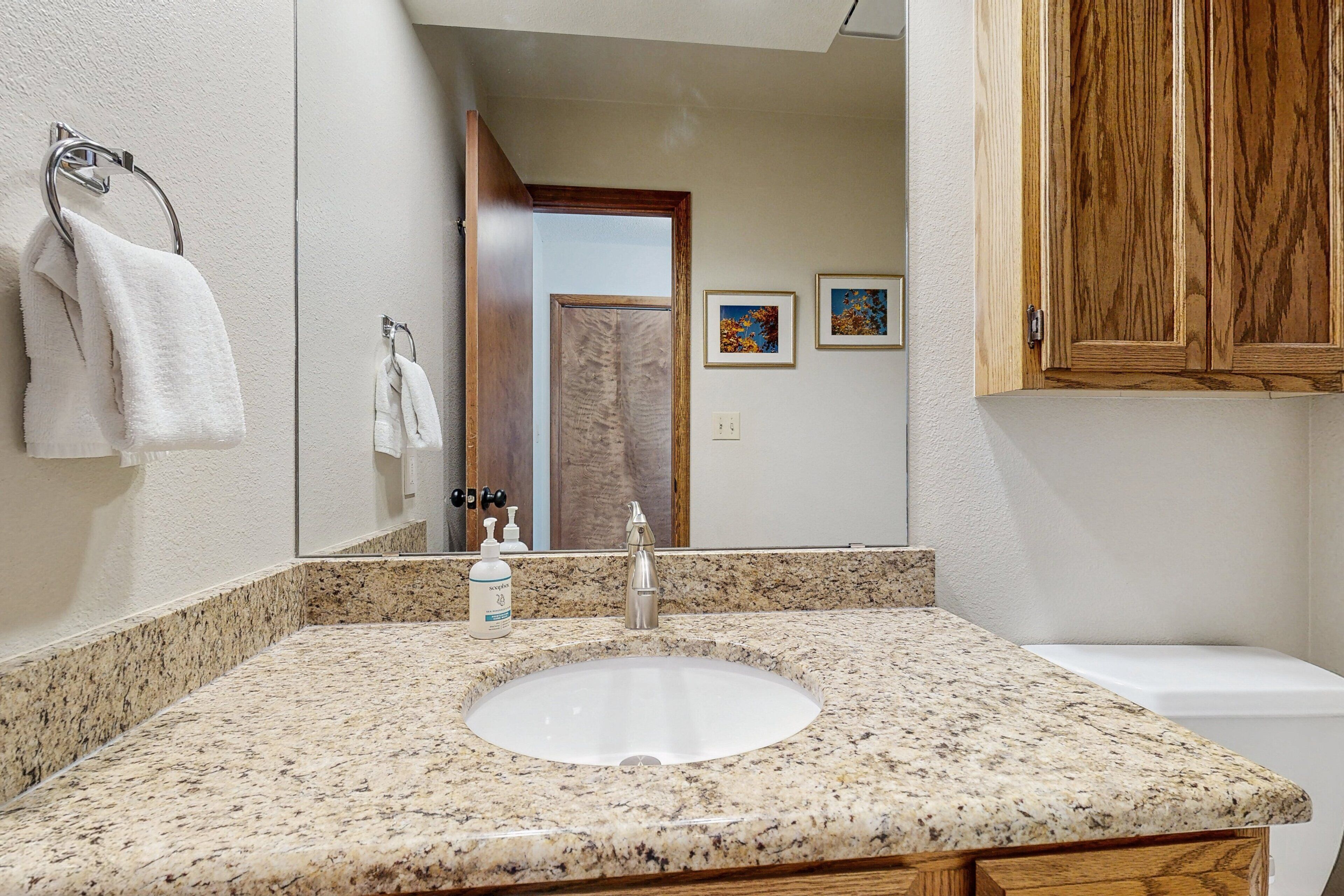 A bathroom with a granite countertop, a white sink, a wooden cabinet, and a mirror reflecting the room.