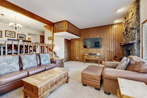 A cozy living room with a wooden wall, a fireplace, a large TV, and a brown leather sofa. - Comfortable Home With Breathtaking Mountain Views and High-speed Wifi (Estes Park)