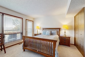A bedroom with a wooden bed, two bedside lamps, a nightstand, a wooden wardrobe, and a window with blinds. - Comfortable Home With Breathtaking Mountain Views and High-speed Wifi (Estes Park)