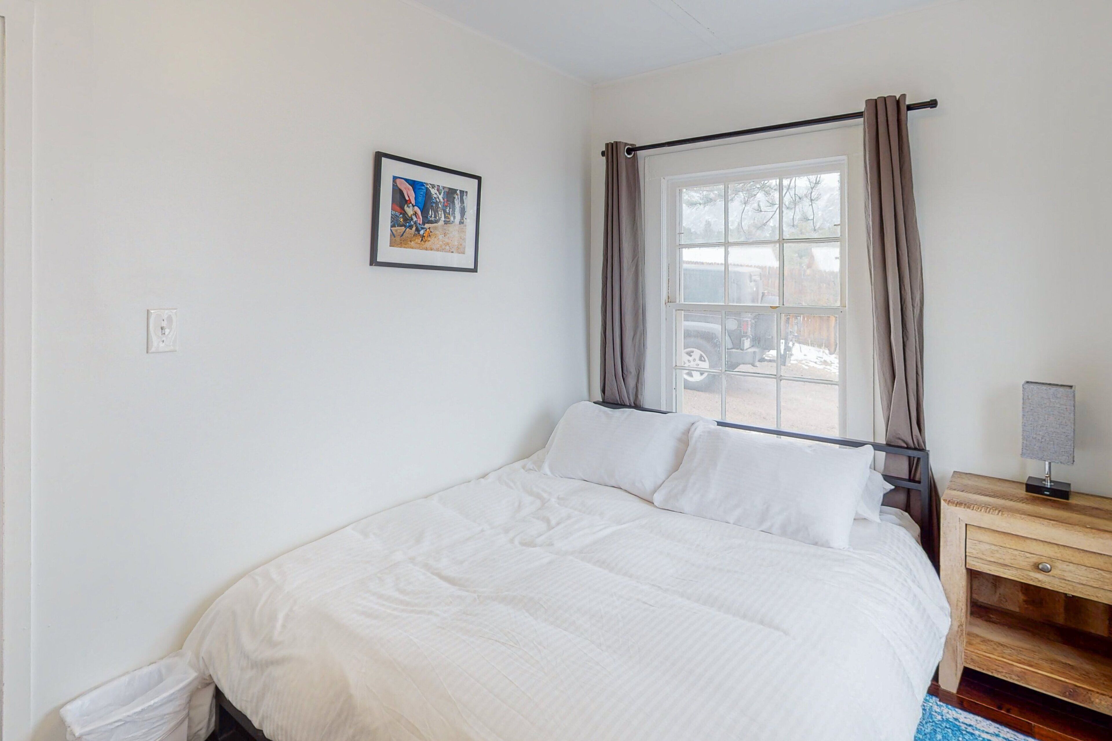 Une chambre à coucher avec un lit, une table de chevet, une fenêtre avec des rideaux et un tableau accroché au mur.