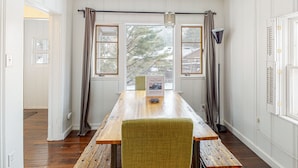Ein Zimmer mit Holztisch, zwei Stühlen, einem Willkommensschild und Blick auf Bäume durch große Fenster.
