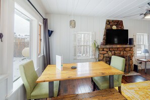 Ein Essbereich mit Holztisch und grünen Stühlen, einem Kamin aus Stein und einem Fernseher an der Wand.