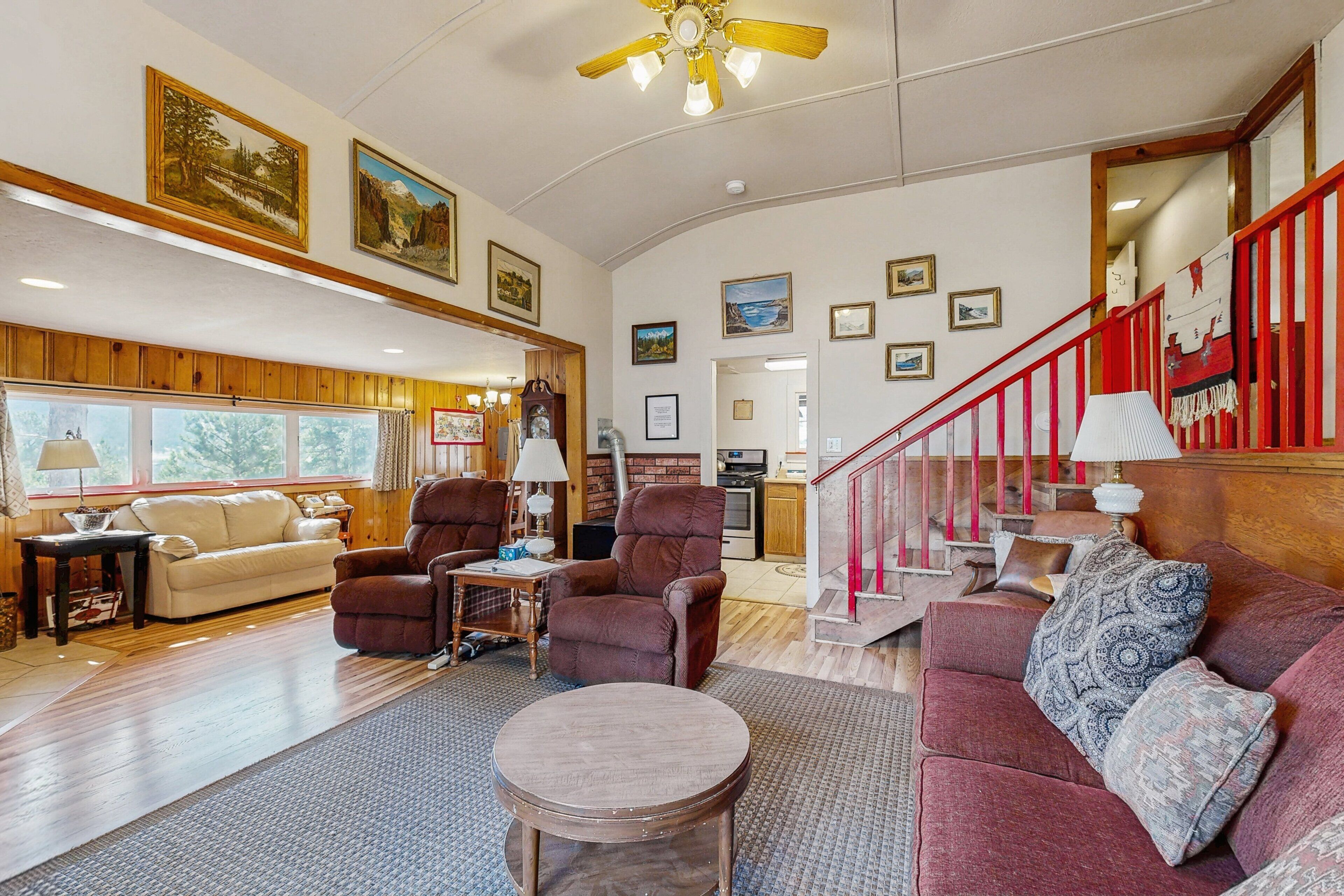 A spacious living room with a wooden floor, a red couch, a round coffee table, and a staircase with red railings.