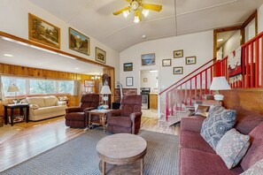 Ein geräumiges Wohnzimmer mit Holzboden, einer roten Couch, einem runden Couchtisch und einer Treppe mit roten Geländern.