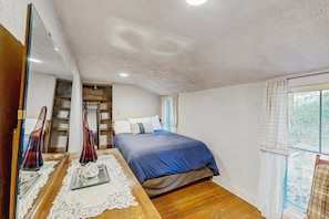 Ein Schlafzimmer mit einem Bett, einem Holzschrank, einem Spiegel und einem Fenster mit Vorhängen.
