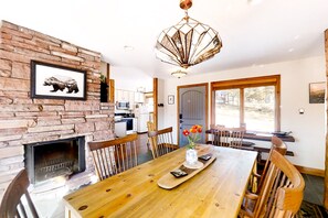 A dining area with a wooden table, chairs, a fireplace, and a large window. - Delightful Getaway With Free Wifi, a Wood Fireplace, Washer/dryer, & Great Views (Estes Park)