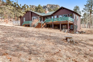 A two-story wooden house with a green balcony, a stone staircase, and a clear view of the surrounding dry grassland and trees. - Delightful Getaway With Free Wifi, a Wood Fireplace, Washer/dryer, & Great Views (Estes Park)