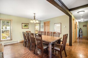 Ein Esszimmer mit einem großen Holztisch und Stühlen, einer Chandelüster und Blick durch ein Fenster.