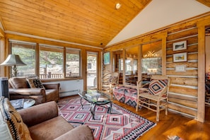 Ein gemütliches Blockhaus-Interieur mit Ledersofa, Glastisch und einem gemusterten Teppich.