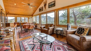 A spacious living room with a high ceiling, wooden beams, large windows, and a mountain view. - Historic Cabin With Mountain Views, Private W/d, & Furnished Deck (Estes Park)