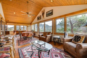 A spacious living room with a high ceiling, wooden beams, large windows, and a mountain view. - Historic Cabin With Mountain Views, Private W/d, & Furnished Deck (Estes Park)