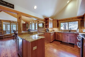 A spacious kitchen with wooden cabinets, a large island, and a view of the outdoors. - Historic Cabin With Mountain Views, Private W/d, & Furnished Deck (Estes Park)