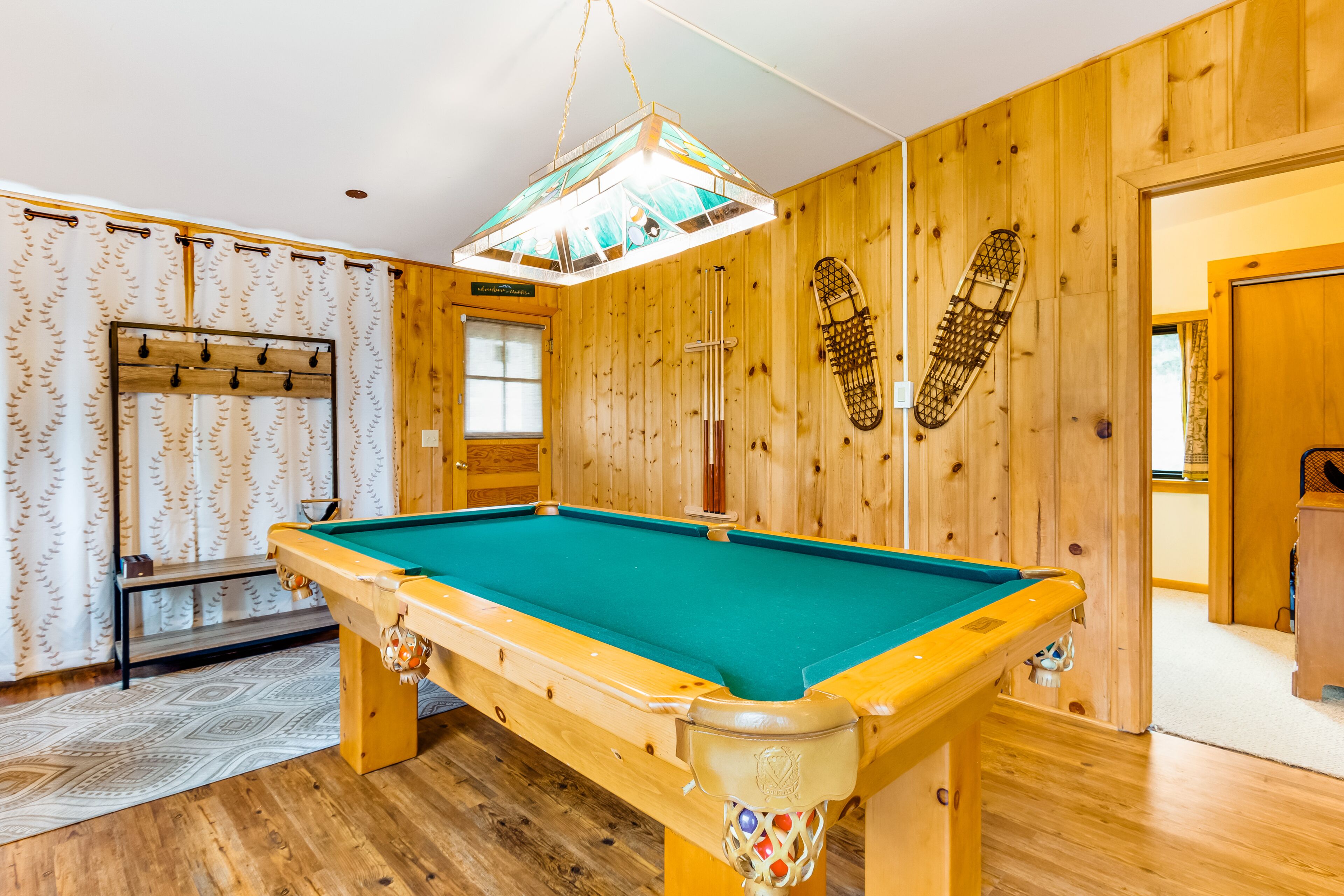 A pool table in a room with wooden walls and a patterned curtain.