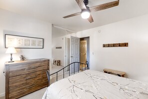 Ein Schlafzimmer mit Bett, Kommode, Deckenventilator und einer Tür zu einem anderen Raum.