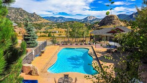 Una piscina con vistas a montañas, un porche cubierto con mobiliario exterior y un área cercada.