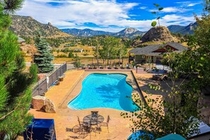 Ein Pool mit Blick auf die Berge, eine überdachte Terrasse mit Gartenmöbeln und ein umzäunter Bereich.