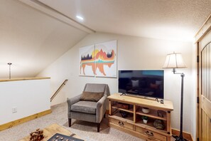 Ein Wohnzimmer mit Fernseher, einem Sessel, einer Lampe und Kunstwerken an der Wand.