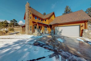 Ein großes, mehrgeschossiges Haus mit einem Steinkamin, einer Garage und einer Auffahrt mit Schneeflecken.