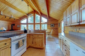 Ein Interieur einer Holzhütte mit Küche, Essbereich und großen Fenstern.